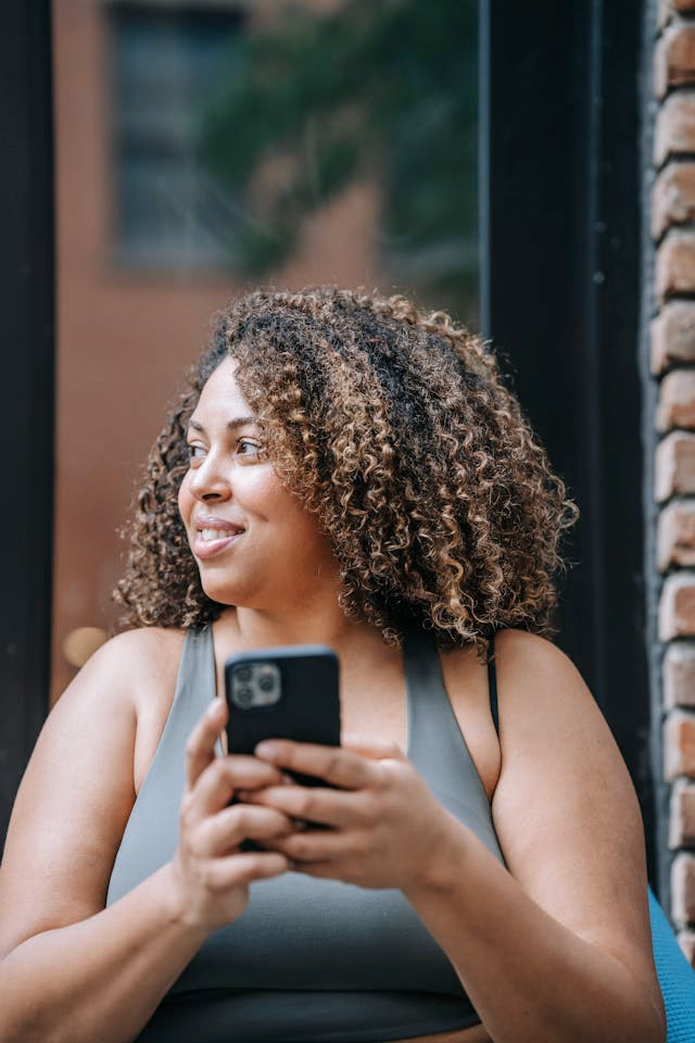 Woman in Sports Clothing Using Her Phone and Smiling