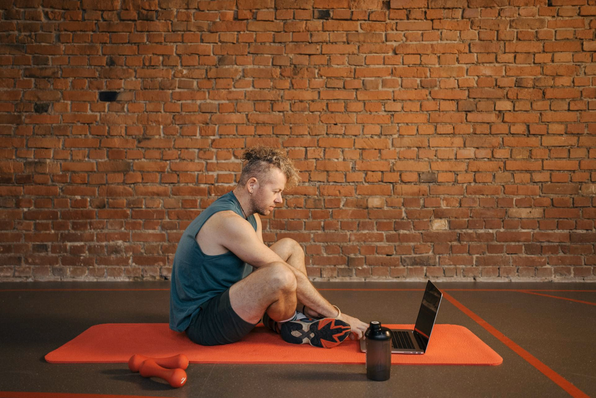 Man Sitting on Exercise Mat While Using Laptop